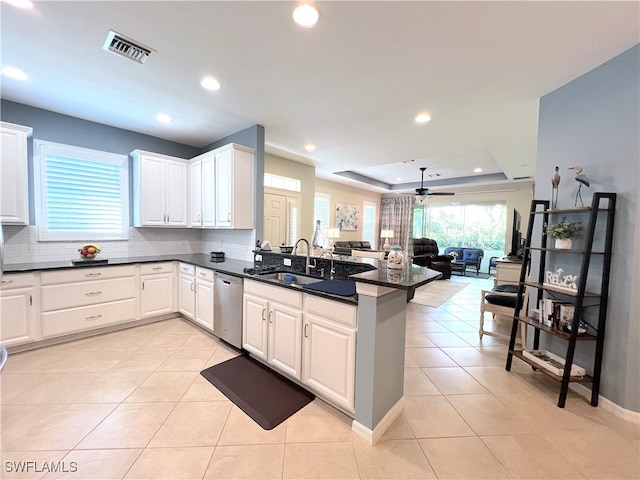 kitchen with kitchen peninsula, sink, stainless steel dishwasher, a tray ceiling, and white cabinetry