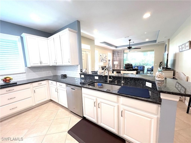 kitchen featuring kitchen peninsula, sink, stainless steel dishwasher, dark stone countertops, and white cabinetry