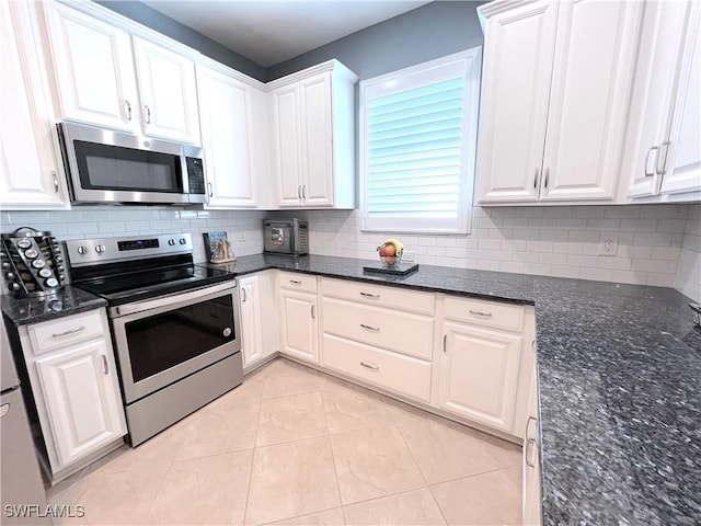 kitchen featuring appliances with stainless steel finishes, tasteful backsplash, dark stone counters, light tile patterned floors, and white cabinets