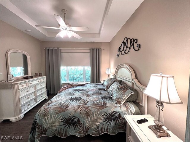 bedroom featuring ceiling fan, dark hardwood / wood-style flooring, a raised ceiling, and multiple windows