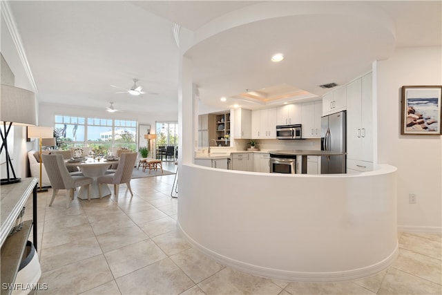 kitchen with stainless steel appliances, ceiling fan, crown molding, white cabinetry, and light tile patterned flooring