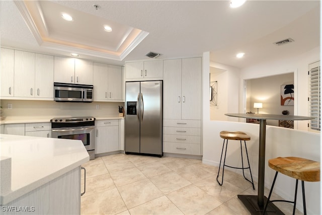 kitchen featuring white cabinets, stainless steel appliances, a raised ceiling, and a breakfast bar area