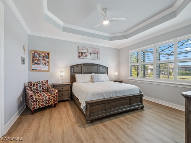 bedroom featuring a tray ceiling, ceiling fan, ornamental molding, and light wood-type flooring