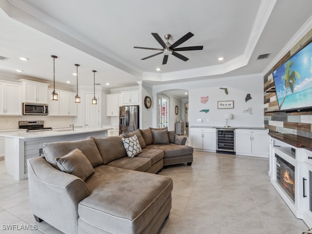 tiled living room featuring a raised ceiling, sink, ceiling fan, ornamental molding, and beverage cooler