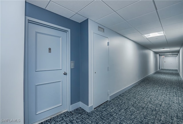 hallway with dark carpet and a drop ceiling