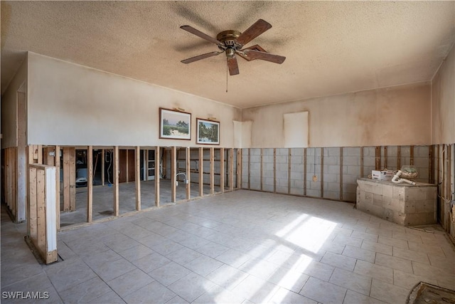 spare room with a textured ceiling, ceiling fan, and tile walls