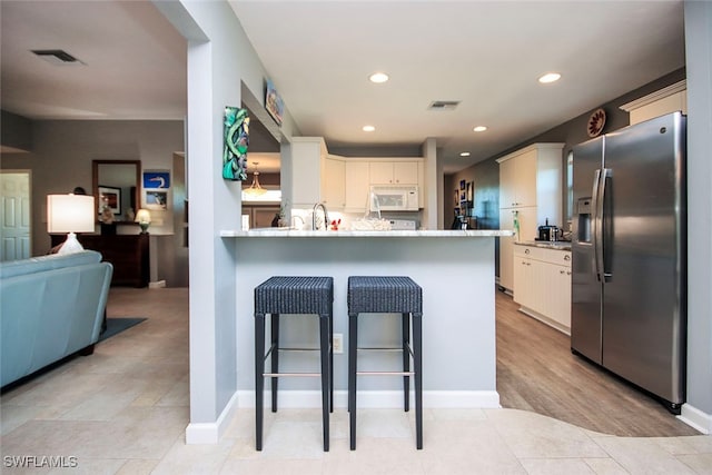 kitchen featuring light stone counters, light hardwood / wood-style flooring, stainless steel refrigerator with ice dispenser, kitchen peninsula, and a kitchen bar