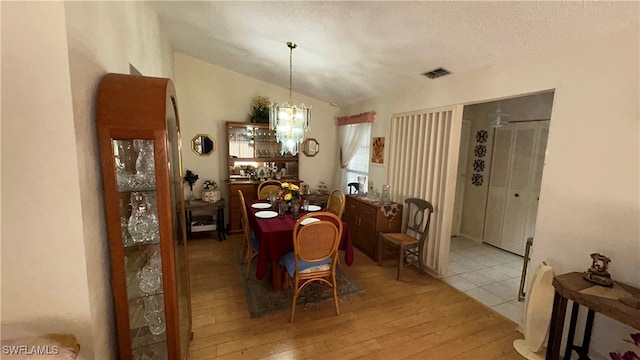 dining space with light hardwood / wood-style floors, lofted ceiling, and a notable chandelier