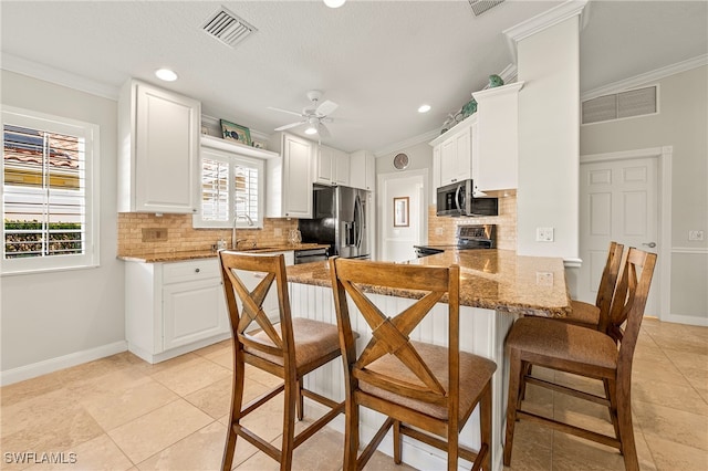 kitchen with kitchen peninsula, decorative backsplash, ornamental molding, white cabinetry, and stainless steel appliances