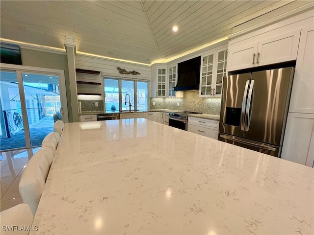 kitchen featuring sink, white cabinets, stainless steel appliances, light stone countertops, and custom range hood