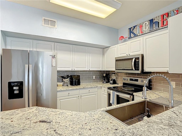 kitchen with sink, appliances with stainless steel finishes, tasteful backsplash, light stone counters, and white cabinetry