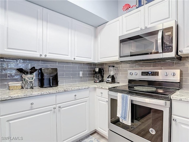 kitchen with appliances with stainless steel finishes, backsplash, white cabinetry, and light stone counters