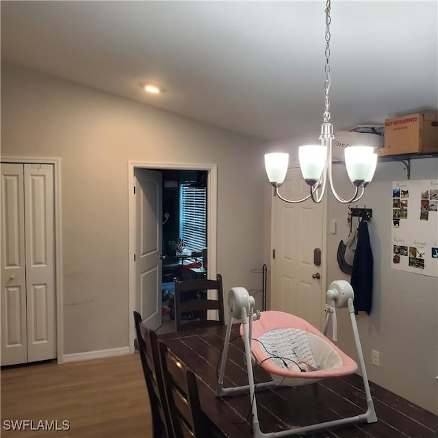 dining space with hardwood / wood-style floors, vaulted ceiling, and an inviting chandelier