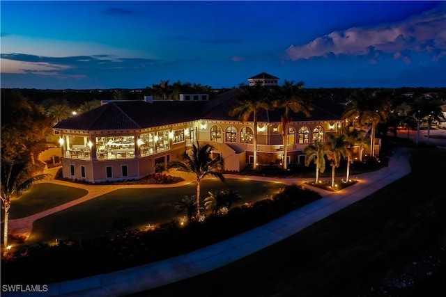 back house at dusk featuring a lawn and a balcony