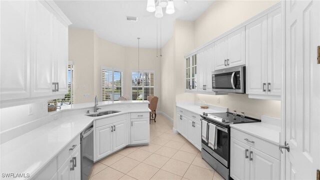 kitchen with light tile patterned floors, a sink, stainless steel appliances, white cabinets, and a chandelier