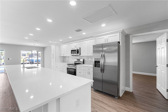 kitchen with a large island with sink, white cabinets, sink, light wood-type flooring, and stainless steel appliances