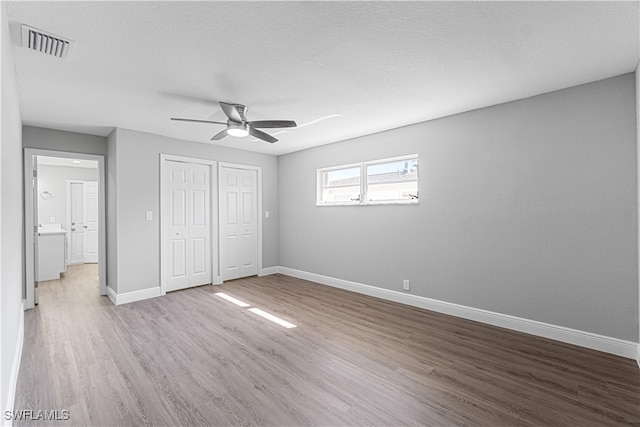 unfurnished bedroom with ceiling fan, two closets, a textured ceiling, and light hardwood / wood-style flooring