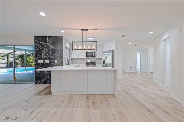 kitchen featuring kitchen peninsula, light hardwood / wood-style flooring, pendant lighting, and appliances with stainless steel finishes