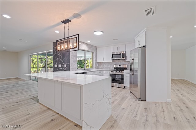 kitchen featuring white cabinets, light stone countertops, appliances with stainless steel finishes, decorative light fixtures, and light hardwood / wood-style floors