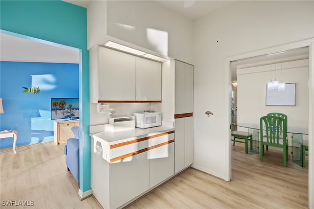 kitchen featuring a chandelier, white cabinetry, hanging light fixtures, and light wood-type flooring