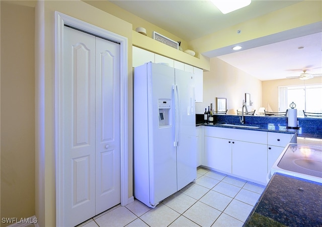 kitchen featuring ceiling fan, white fridge with ice dispenser, sink, white cabinets, and range