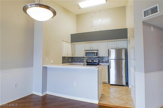 kitchen with tasteful backsplash, kitchen peninsula, appliances with stainless steel finishes, white cabinets, and light wood-type flooring