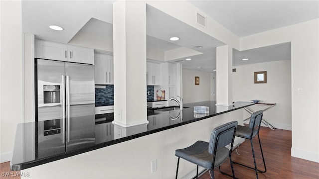 kitchen with kitchen peninsula, tasteful backsplash, white cabinetry, and high end fridge