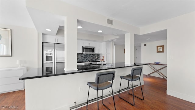 kitchen with backsplash, wood-type flooring, white cabinetry, and stainless steel appliances