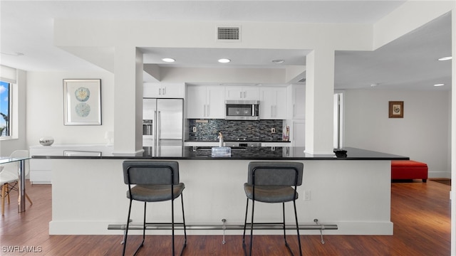 kitchen featuring appliances with stainless steel finishes, dark hardwood / wood-style floors, white cabinetry, and a kitchen breakfast bar