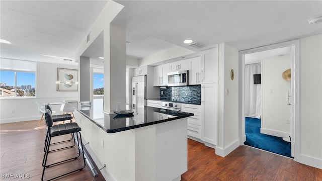 kitchen featuring dark wood-type flooring, stainless steel appliances, a kitchen breakfast bar, backsplash, and white cabinets