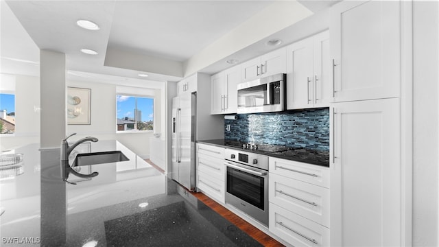 kitchen with dark wood-type flooring, white cabinets, decorative backsplash, dark stone countertops, and stainless steel appliances