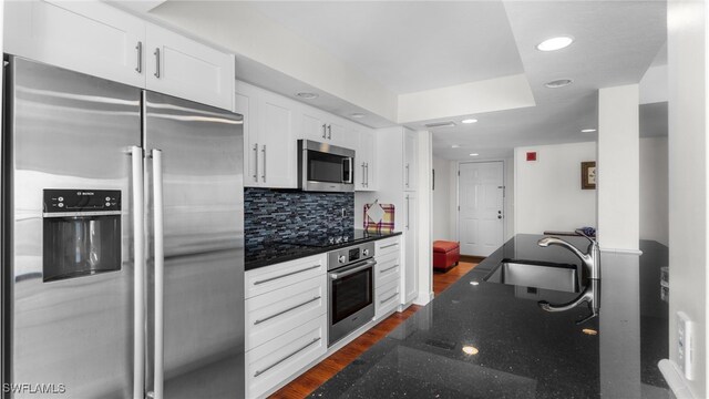 kitchen with sink, dark hardwood / wood-style floors, dark stone countertops, white cabinetry, and stainless steel appliances