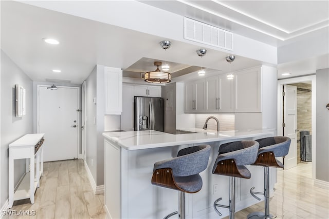 kitchen featuring kitchen peninsula, a tray ceiling, sink, white cabinets, and stainless steel fridge with ice dispenser