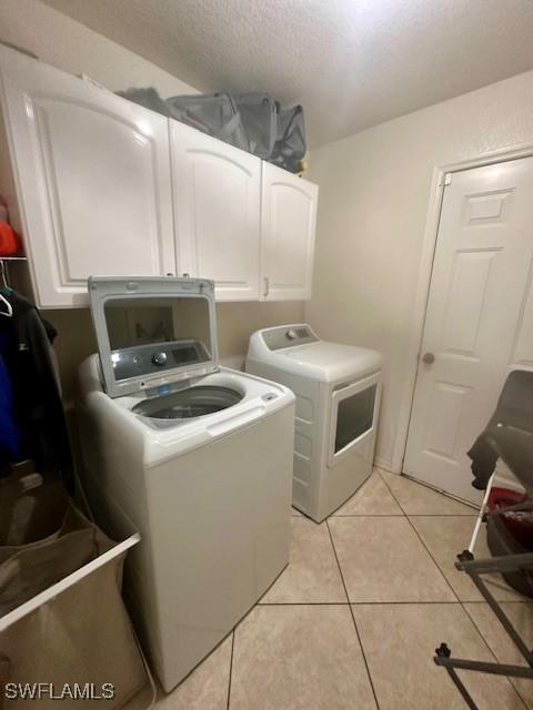 laundry area featuring washing machine and clothes dryer, light tile patterned flooring, cabinets, and a textured ceiling