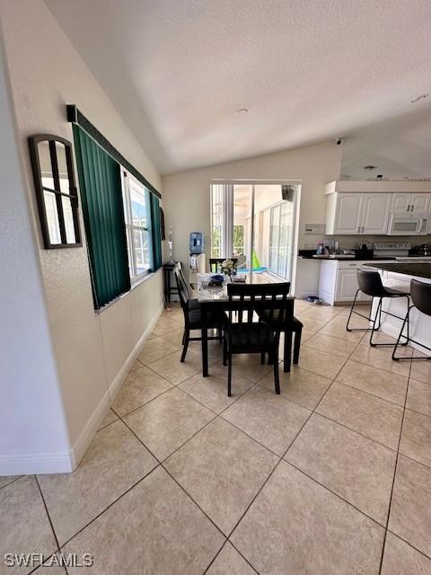 dining area with light tile patterned floors, a textured ceiling, and vaulted ceiling