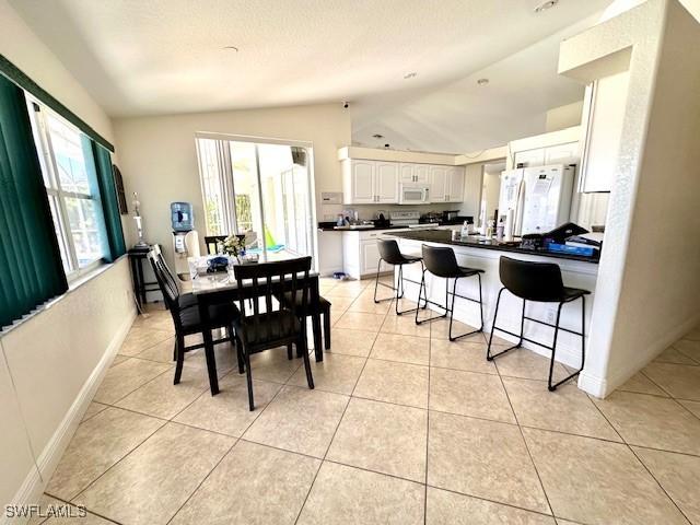 dining area featuring plenty of natural light, light tile patterned floors, and vaulted ceiling