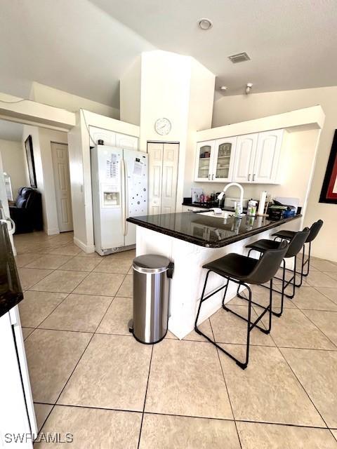 kitchen featuring white cabinetry, sink, white refrigerator with ice dispenser, lofted ceiling, and a breakfast bar