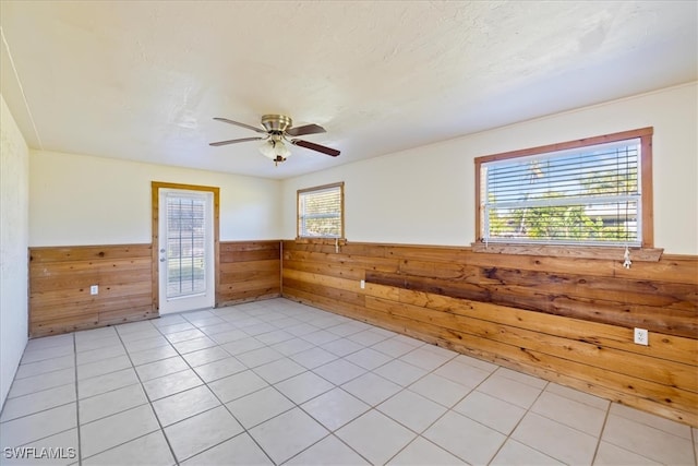 tiled spare room featuring wooden walls and ceiling fan