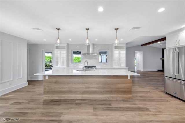 381 Norwood Ct, Fort Myers, FL 33919 - kitchen with high end fridge, wall chimney exhaust hood, white cabinets, a sink, and a center island with sink