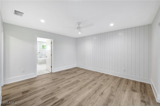 empty room with ceiling fan, light hardwood / wood-style flooring, and wood walls