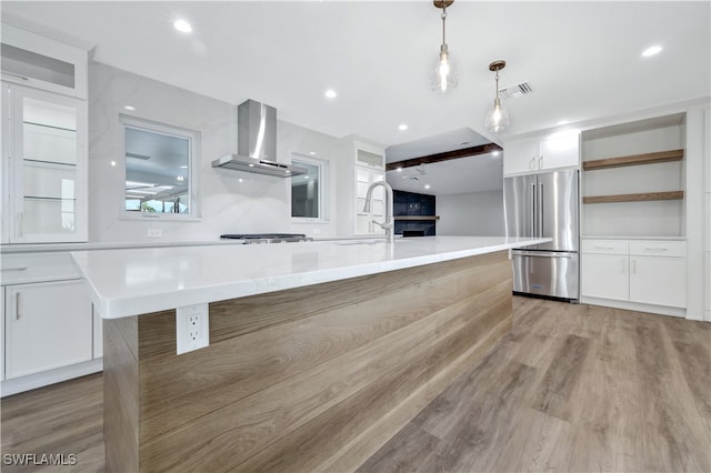 kitchen featuring pendant lighting, a spacious island, wall chimney range hood, white cabinetry, and stainless steel appliances