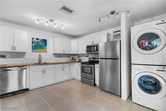 kitchen featuring appliances with stainless steel finishes, white cabinetry, and stacked washer / dryer