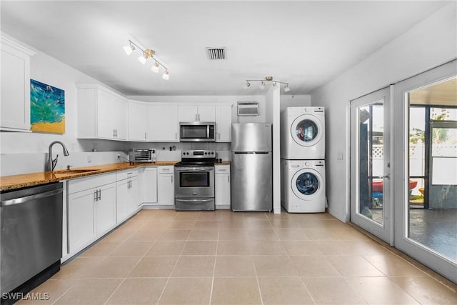 kitchen with stacked washer / dryer, white cabinets, stainless steel appliances, and light tile patterned floors