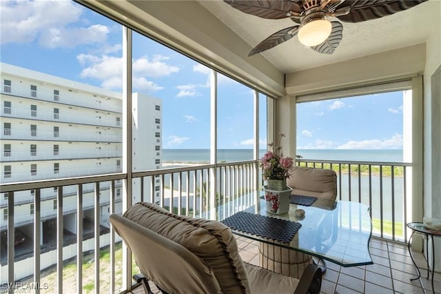 sunroom featuring a water view, ceiling fan, and a view of the beach