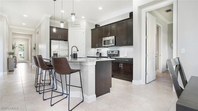 kitchen with decorative light fixtures, sink, stainless steel appliances, dark brown cabinets, and a center island with sink