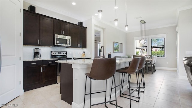 kitchen featuring light stone countertops, a kitchen breakfast bar, stainless steel appliances, a center island with sink, and hanging light fixtures