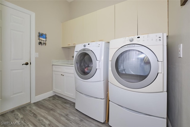 washroom featuring washer and clothes dryer, cabinets, and light hardwood / wood-style flooring