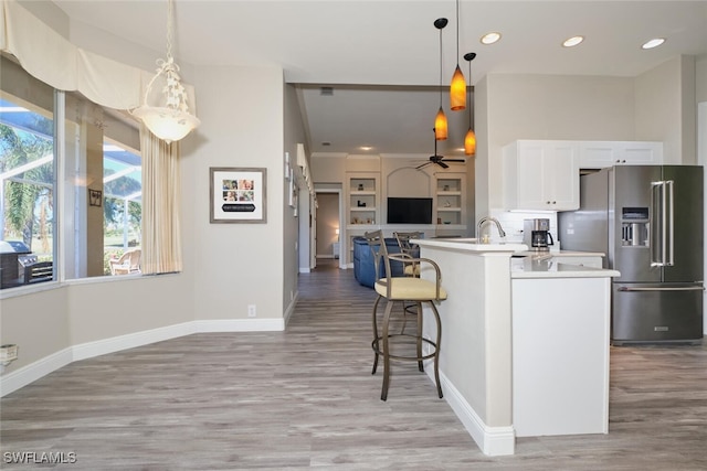 kitchen with high end fridge, white cabinetry, hanging light fixtures, and light hardwood / wood-style flooring