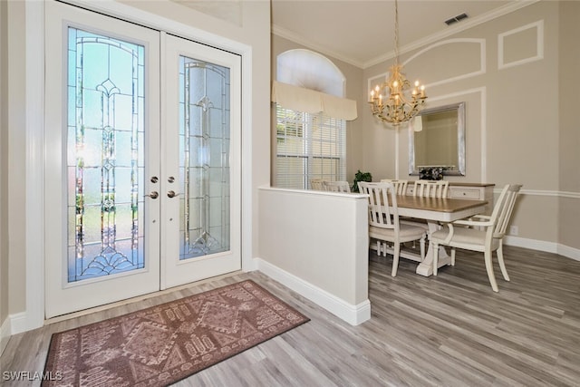 entrance foyer with hardwood / wood-style floors, a notable chandelier, crown molding, and french doors