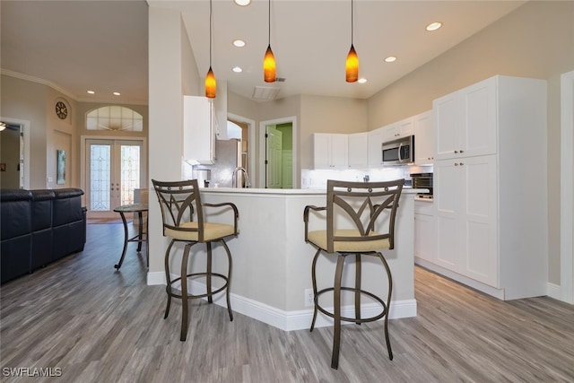 kitchen with appliances with stainless steel finishes, light wood-type flooring, french doors, a kitchen breakfast bar, and white cabinetry